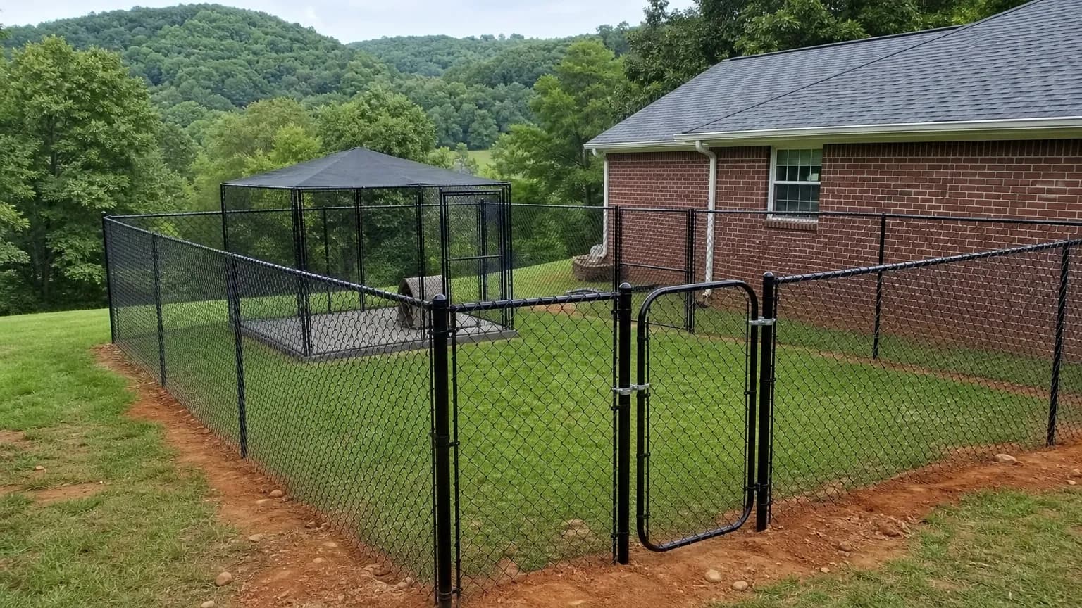 Black vinyl-coated chain link dog yard beside a brick ranch house with a covered 10x10 kennel run in the corner