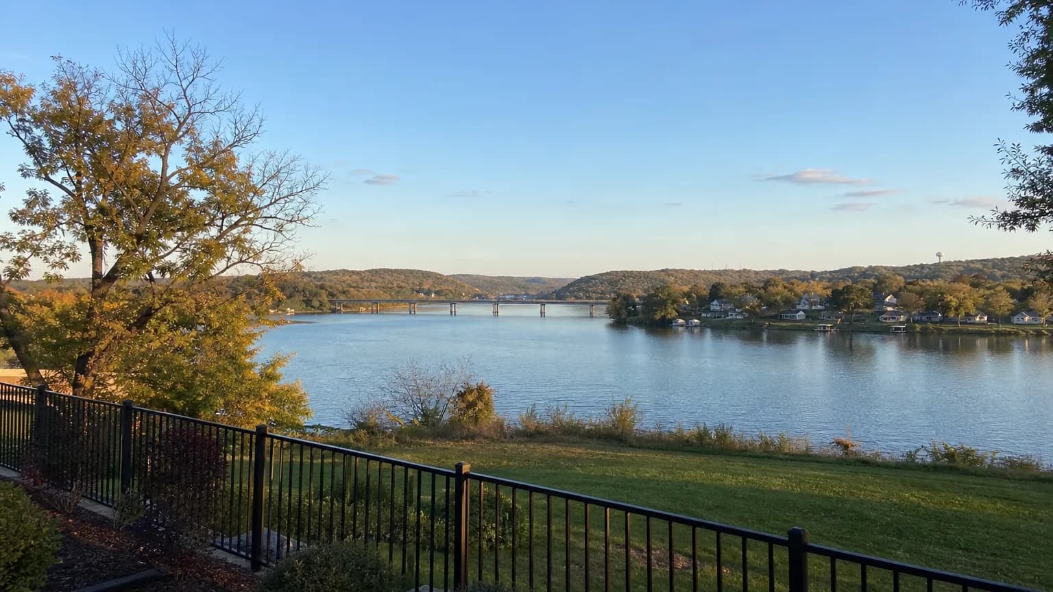 Wide view of the Tennessee River from a bluff with a backyard aluminum fence in the foreground in late afternoon light
